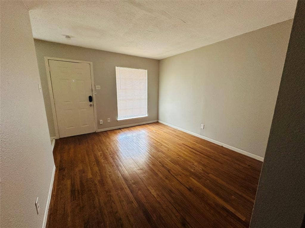 5317 Junius Street, #212, Dallas, TX 75214 Room featuring wood-finish flooring, neutral wall paint, a six-panel entry door, and a window with integrated blinds
