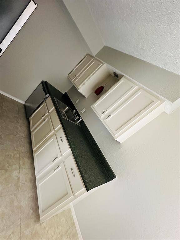 5317 Junius Street, #212, Dallas, TX 75214 Kitchenette featuring shaker-style cabinetry, dark stone-finish countertops, stainless steel sink, and ceramic tile flooring