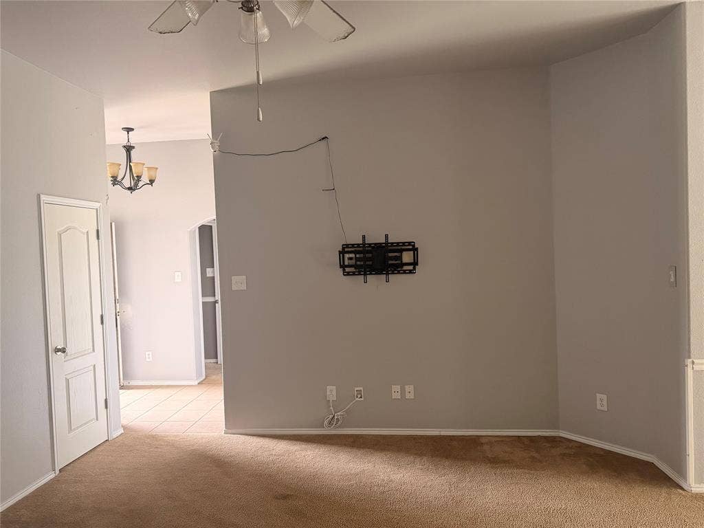705 Bamboo Drive, Anna, TX 75409 Neutral interior space featuring high ceilings, a wall-mounted media bracket, a central ceiling fan with integrated lighting, and a multi-light chandelier