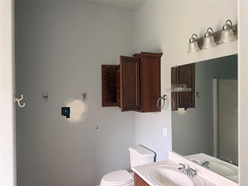 705 Bamboo Drive, Anna, TX 75409 Vanity featuring a white surface, undermount basin, and wood-finish cabinetry, complemented by a large wall-mounted mirror, three-light fixture, and dark wood wall-mounted cabinet