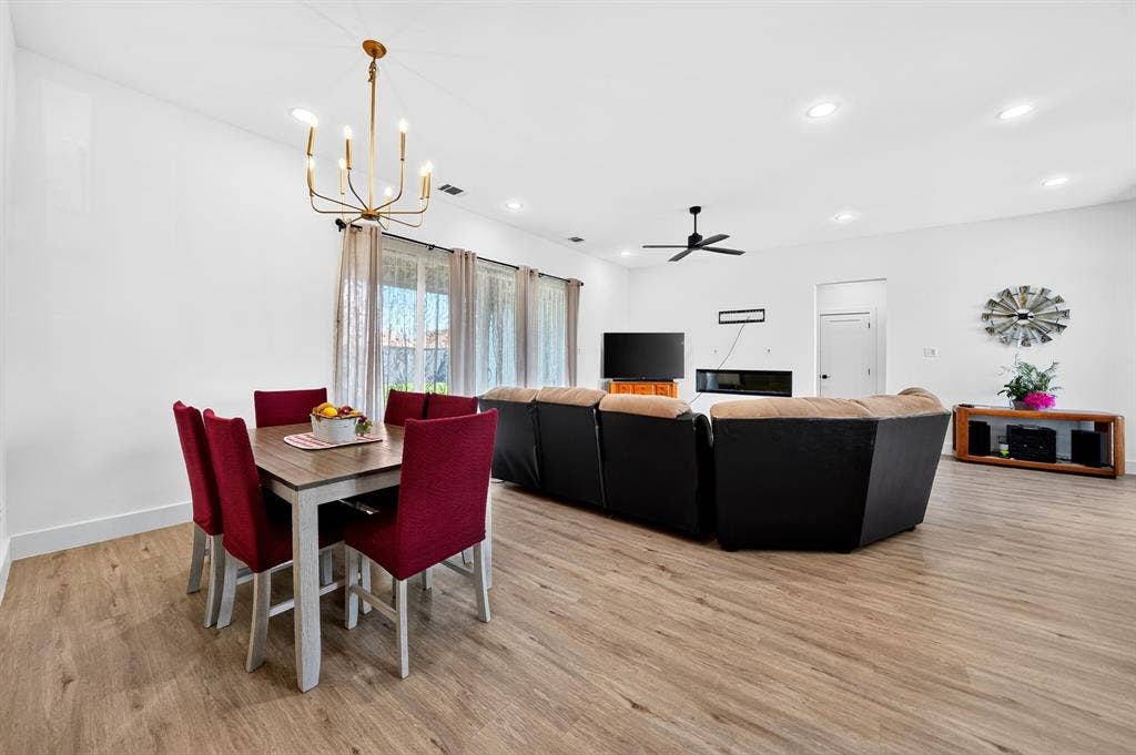 Open-concept interior featuring wood-finish flooring, recessed lighting, a modern candle-style chandelier, and a wall-mounted linear fireplace