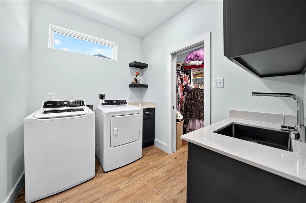 Laundry room featuring wood-finish flooring, a stone-surfaced vanity with an undermount sink, matte black faucet hardware, built-in shelving, and dark cabinetry