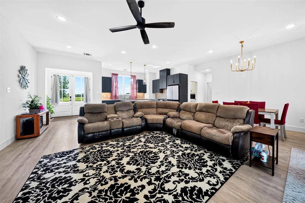 Open-concept main room featuring wood-finish flooring, recessed lighting, a matte black ceiling fan, and a multi-light chandelier