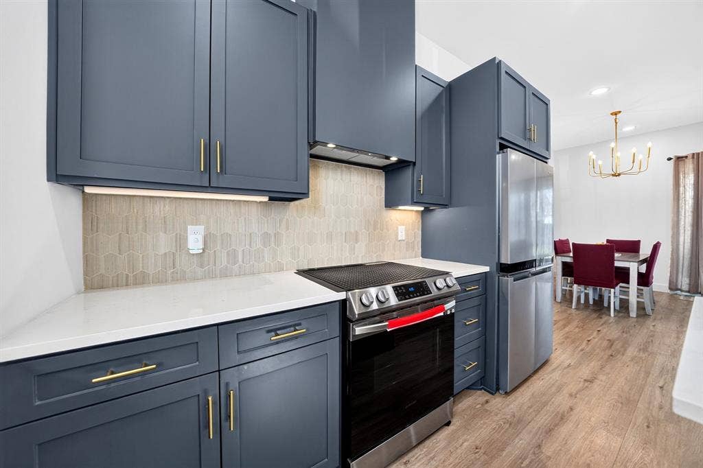 Modern kitchen featuring custom cabinetry with brushed gold hardware, white quartz countertops, subway tile backsplash, stainless steel appliances including a slide-in range, and wood-finish flooring throughout the open-concept space