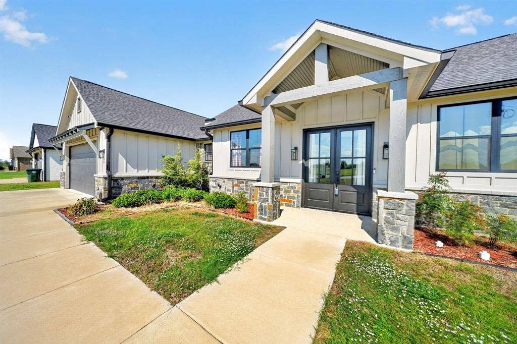 Board-and-batten siding exterior featuring stone veneer accents, a covered front entryway with timber-style posts, and double front entry doors