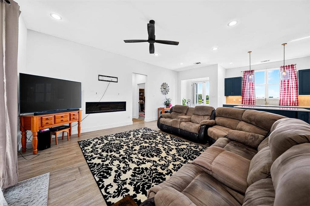 Open-concept living space featuring wood-finish flooring, recessed lighting, a linear wall-mounted electric fireplace, and a ceiling fan with matte black finish