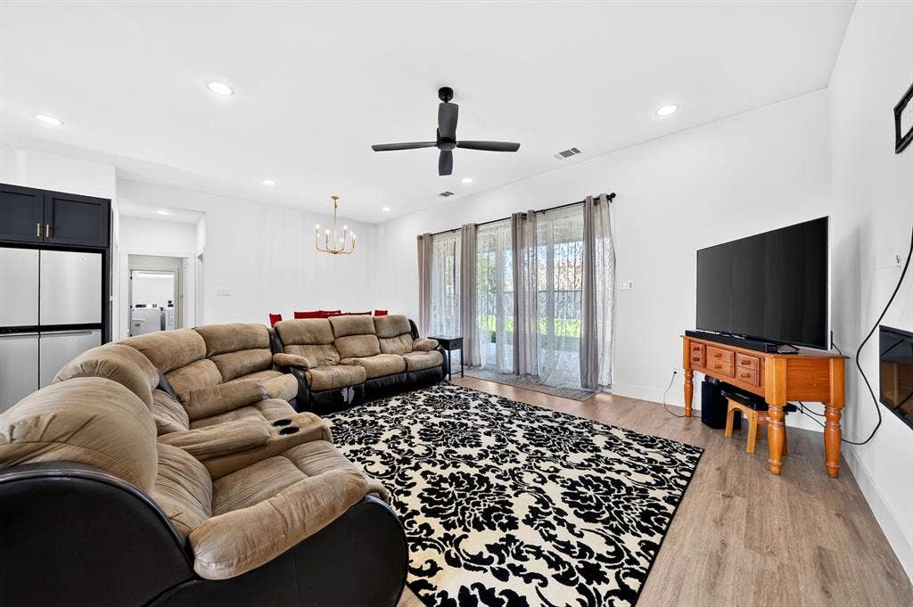 Open-concept living space featuring wood-finish flooring, recessed lighting, a matte black ceiling fan, and large sliding glass doors
