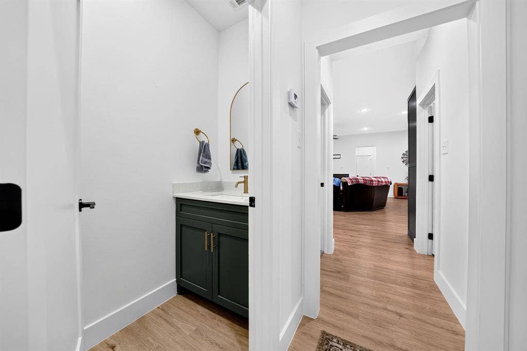 Vanity featuring deep-toned cabinetry, brushed metallic hardware, integrated countertop with sink, and an arched wall-mounted mirror