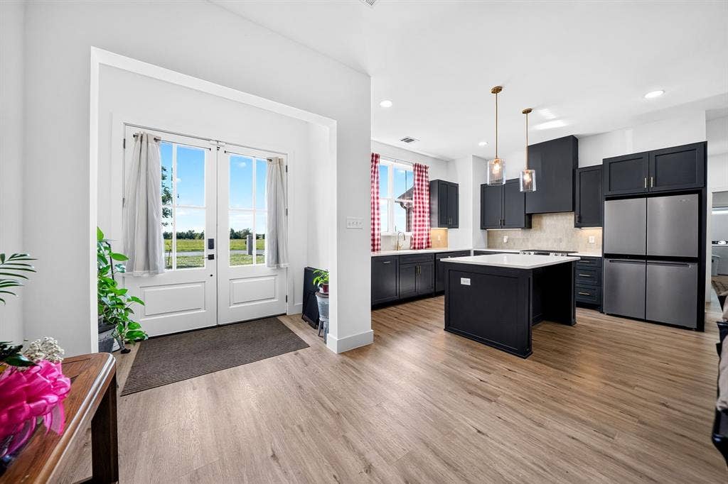 Kitchen featuring dark cabinetry, a central island with a stone countertop, stainless steel refrigerator, recessed lighting, and wood-finish flooring