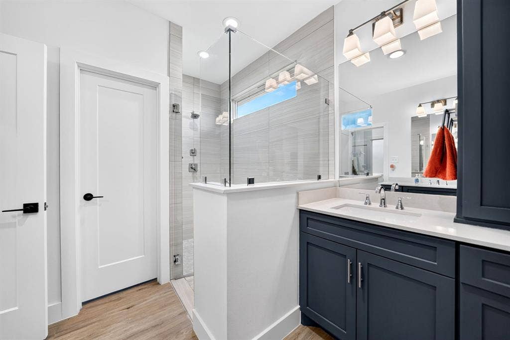 Bathroom featuring a dark-toned vanity with a light-colored countertop, glass-enclosed walk-in shower with horizontal wall tile, wood-finish flooring, and a multi-light fixture