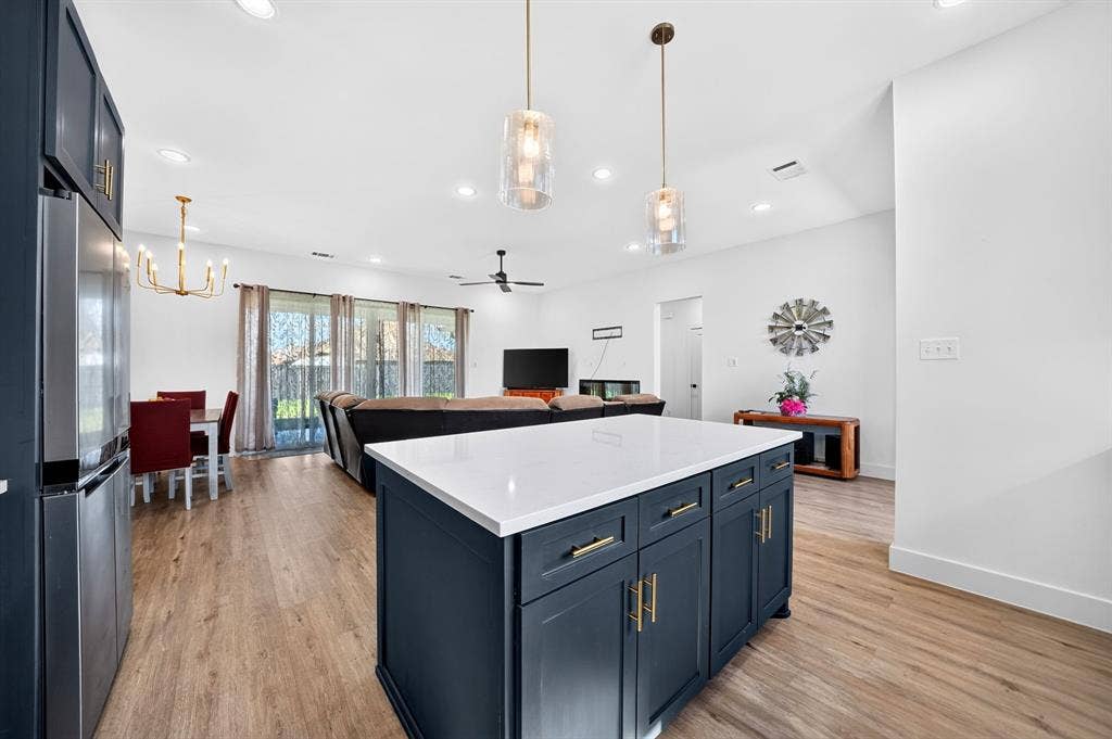 Kitchen featuring a center island with dark cabinetry, white stone-finish countertop, dual pendant lighting, and wood-finish flooring