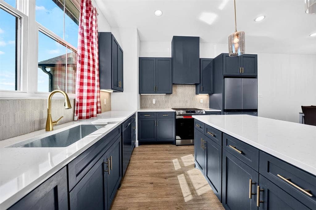 Kitchen featuring deep blue shaker-style cabinetry, quartz countertops, a brass-finish gooseneck faucet, a textured tile backsplash, and wood-finish flooring