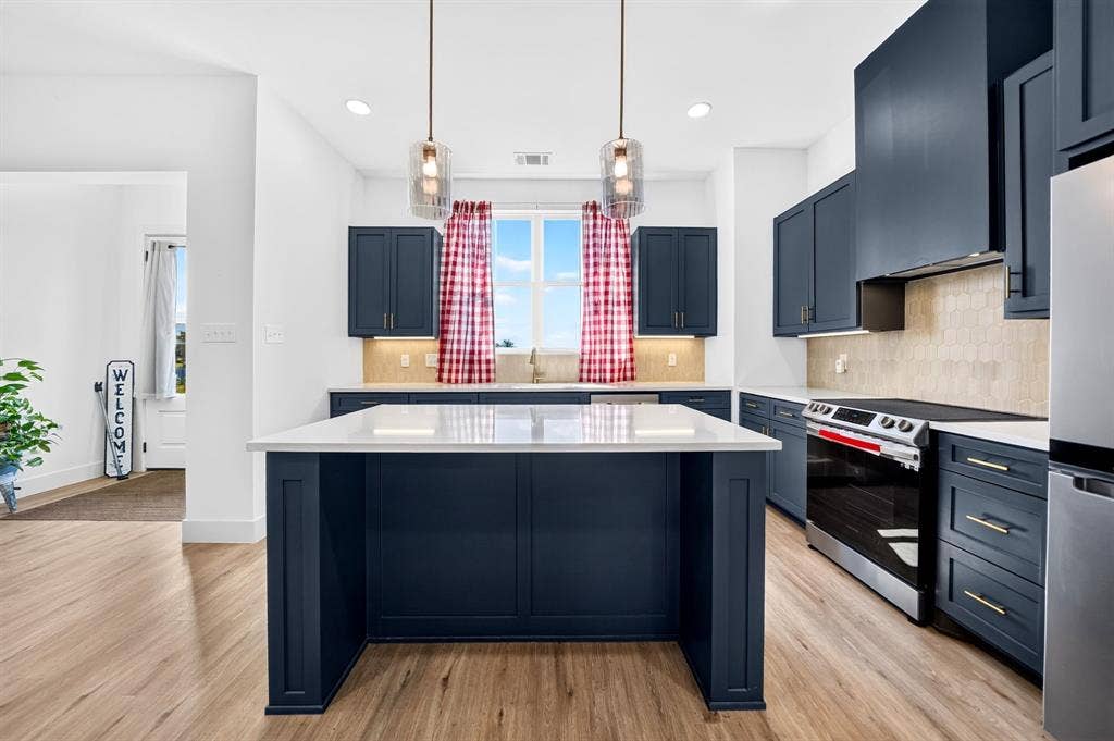 Kitchen featuring navy blue shaker cabinetry, a center island with a white countertop, stainless steel appliances, a tile backsplash, and wood-finish flooring
