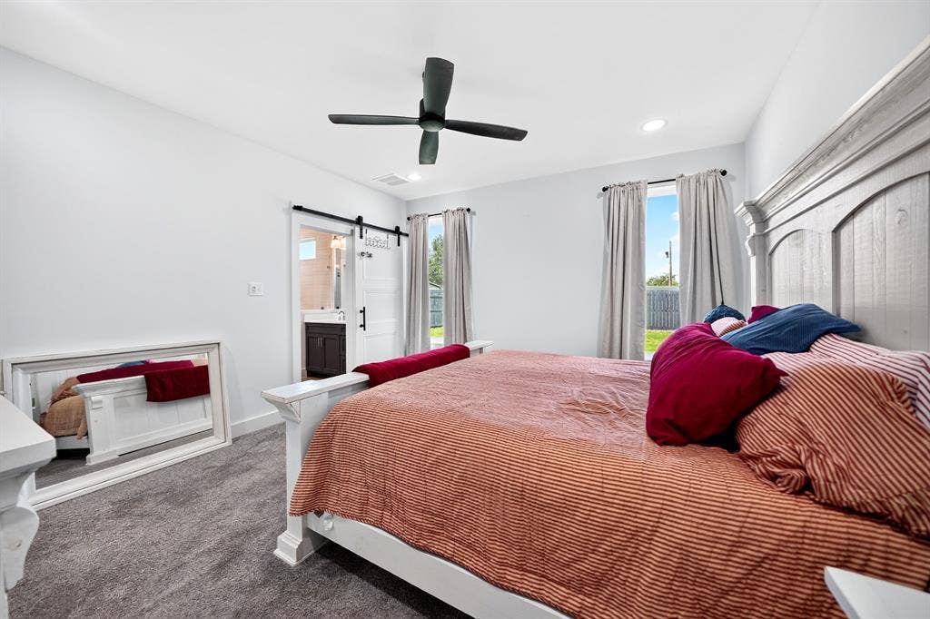 Bedroom featuring gray carpeting, a matte black four-blade ceiling fan, and a white sliding barn door with black iron hardware
