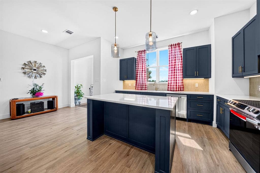 Kitchen featuring deep blue cabinetry, quartz countertops, a central island, wood-finish flooring, and dual glass pendant light fixtures