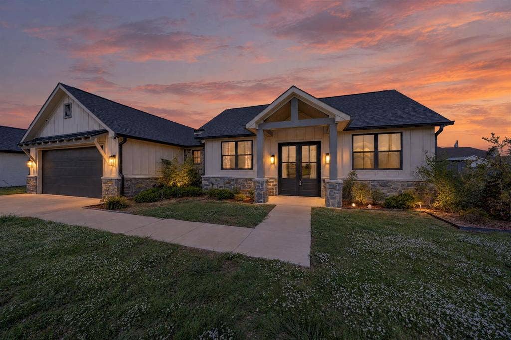 Modern exterior featuring vertical board-and-batten siding, stone veneer accents, gabled roofline, covered front entryway with timber-style columns, and an attached multi-car garage