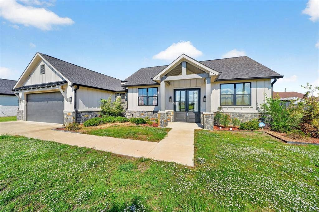 Single-story exterior featuring board-and-batten siding, stone veneer accents, a covered front entryway, double-door entrance, and an attached two-car garage