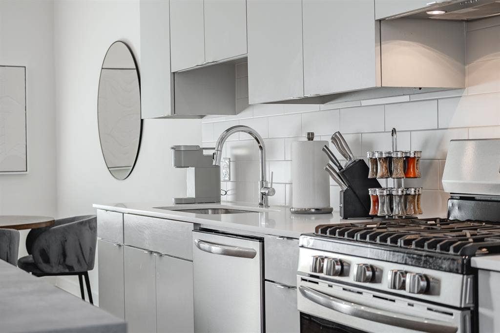 1502 Bennett Avenue, #106, Dallas, TX 75206 Kitchen featuring flat-panel cabinetry, light-toned stone-finish countertops, subway tile backsplash, and stainless steel appliances including a gas range and undermount sink with a gooseneck faucet