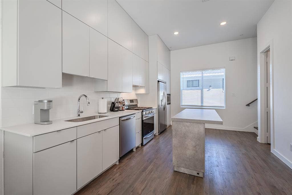 1502 Bennett Avenue, #106, Dallas, TX 75206 Kitchen featuring floor-to-ceiling cabinetry, stainless steel appliances, stone-finish island, wood-finish flooring, and recessed lighting