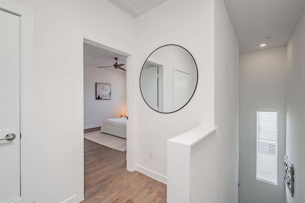 1502 Bennett Avenue, #106, Dallas, TX 75206 Interior hallway featuring wood-finish flooring, a wall-mounted circular mirror with a black frame, and a tall vertical window with integrated blinds