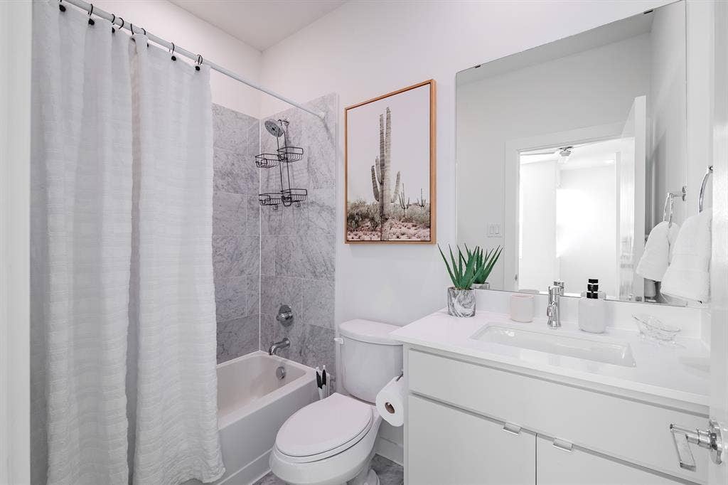 1502 Bennett Avenue, #106, Dallas, TX 75206 Bathroom featuring a white vanity with a composite countertop and integrated sink, a large wall-mounted mirror, and a tub-shower combination with floor-to-ceiling stone-finish tile surround