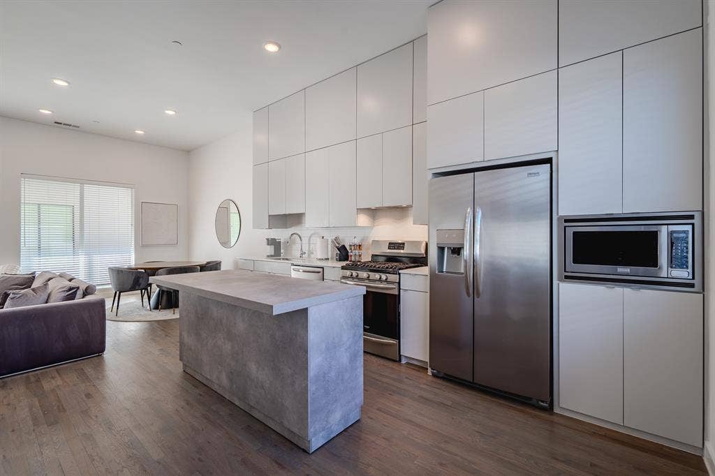 1502 Bennett Avenue, #106, Dallas, TX 75206 Kitchen featuring full-height flat-panel cabinetry, stone-finish kitchen island, stainless steel appliances, and wood-finish flooring