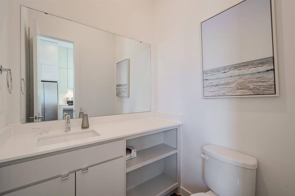 1502 Bennett Avenue, #106, Dallas, TX 75206 Custom vanity featuring a light gray finish, solid-surface countertop with an integrated rectangular sink, polished chrome faucet, and open lower shelving, complemented by a wall-to-wall mirror and chrome towel ring