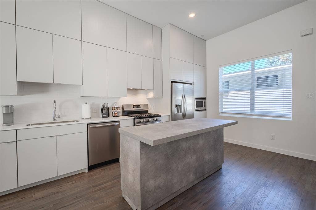 1502 Bennett Avenue, #106, Dallas, TX 75206 Kitchen featuring floor-to-ceiling white cabinetry, wood-finish flooring, a central island with a stone-finish countertop, and stainless steel appliances