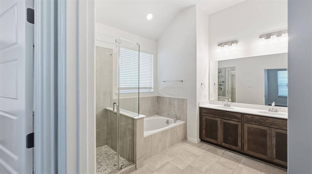 3129 Grayslick Avenue, Celina, TX 75009 Bathroom featuring a dual-sink vanity with dark-finish cabinetry, a large frameless mirror, a deep soaking tub, a tiled walk-in shower with a glass enclosure, and high vaulted ceilings