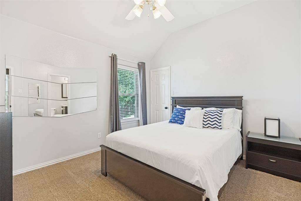 2404 Creek Ridge Drive, McKinney, TX 75072 Vaulted ceiling, wall-mounted segmented mirror, window with neutral drapery, six-panel interior door, and ceiling fan with integrated lighting