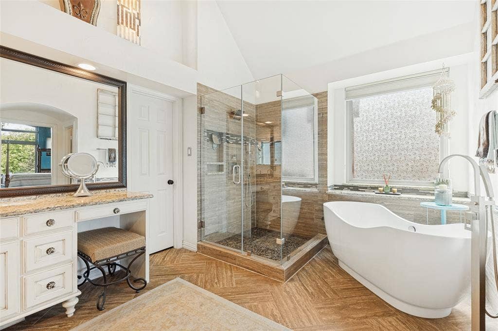2404 Creek Ridge Drive, McKinney, TX 75072 Bathroom featuring a freestanding soaking tub, walk-in glass-enclosed shower with tiled surround, stone-top vanity with built-in cabinetry, and wood-finish herringbone flooring