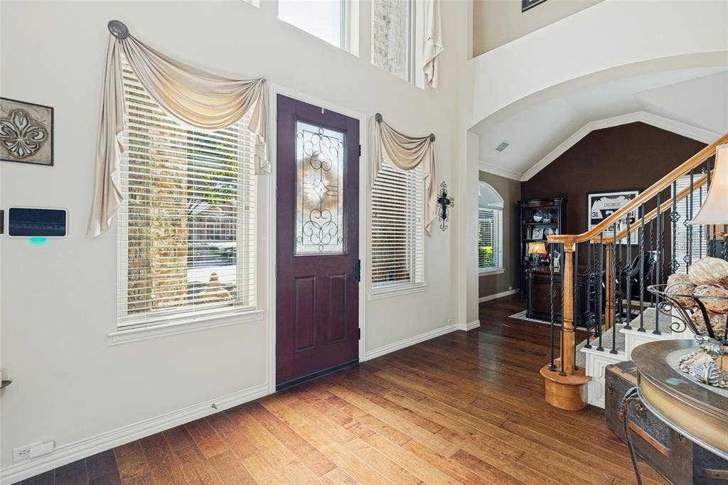 2404 Creek Ridge Drive, McKinney, TX 75072 Two-story foyer with high ceilings, wood-finish flooring, an arched entryway, and a solid wood front door featuring decorative glass inlay, complemented by a staircase with iron balusters and a wood handrail
