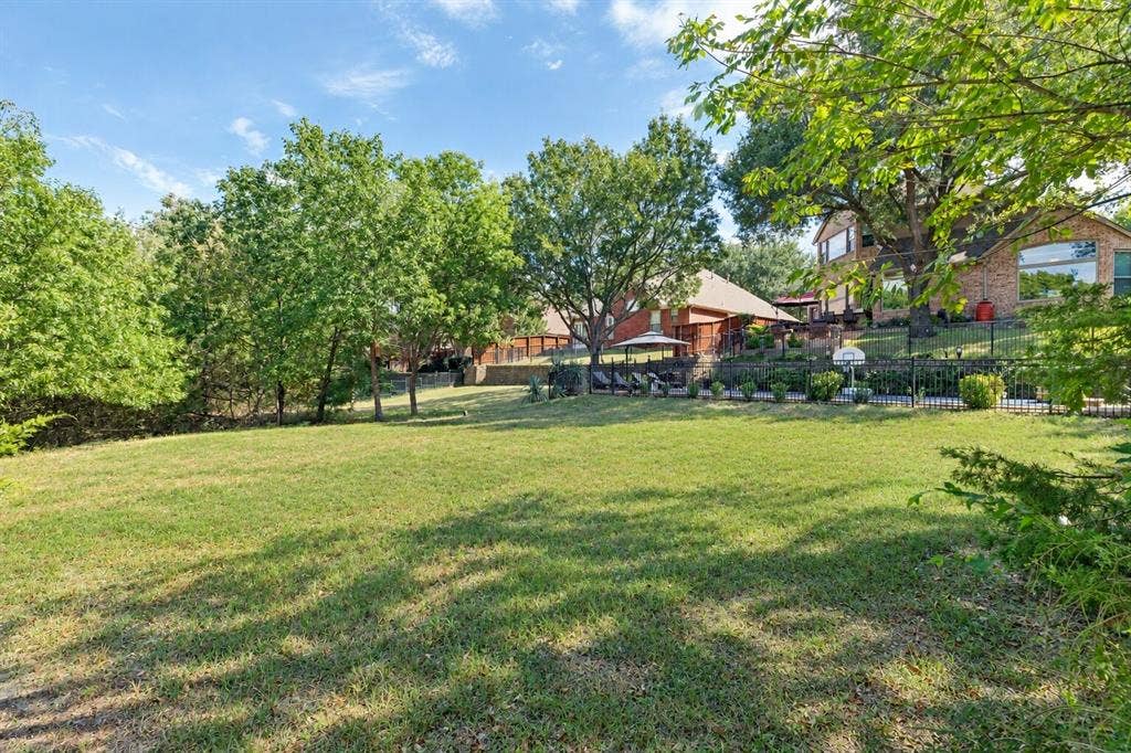 2404 Creek Ridge Drive, McKinney, TX 75072 Expansive backyard featuring a manicured lawn, mature trees, tiered stone retaining walls, and a perimeter metal fence