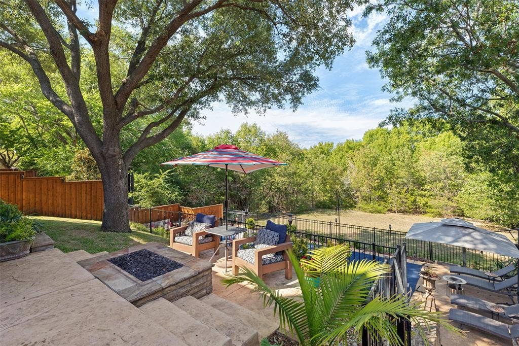 2404 Creek Ridge Drive, McKinney, TX 75072 Tiered stone patio featuring a built-in fire pit, metal perimeter fencing, mature trees, and landscaping