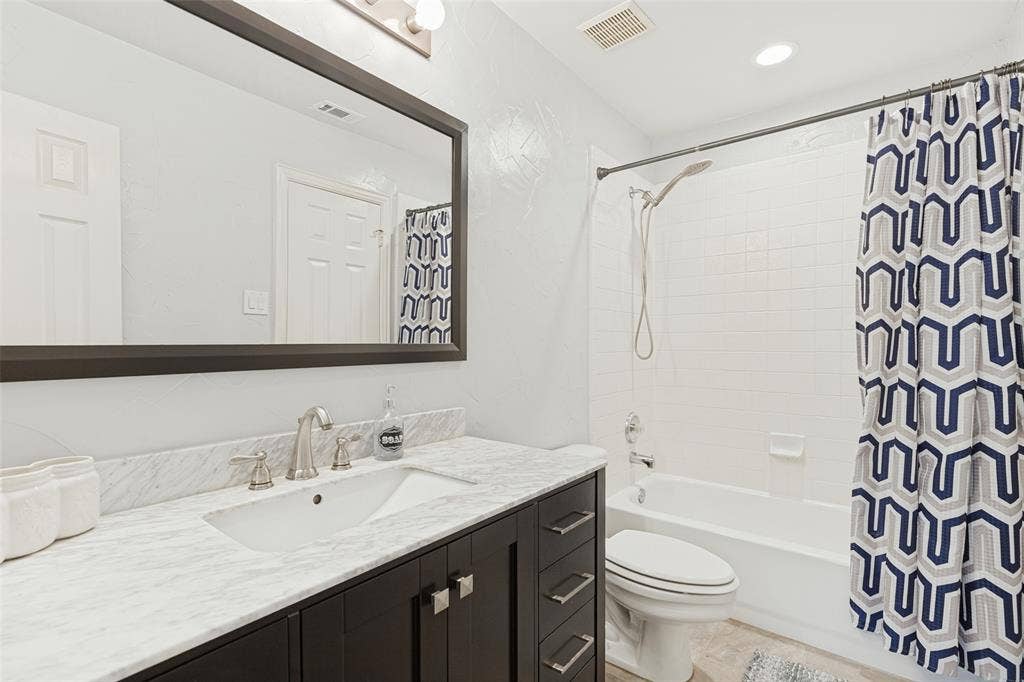 2404 Creek Ridge Drive, McKinney, TX 75072 Dark wood vanity cabinet featuring a stone-top counter, undermount sink with a metallic finish faucet, large framed mirror, and a tub-shower combination with tiled surround