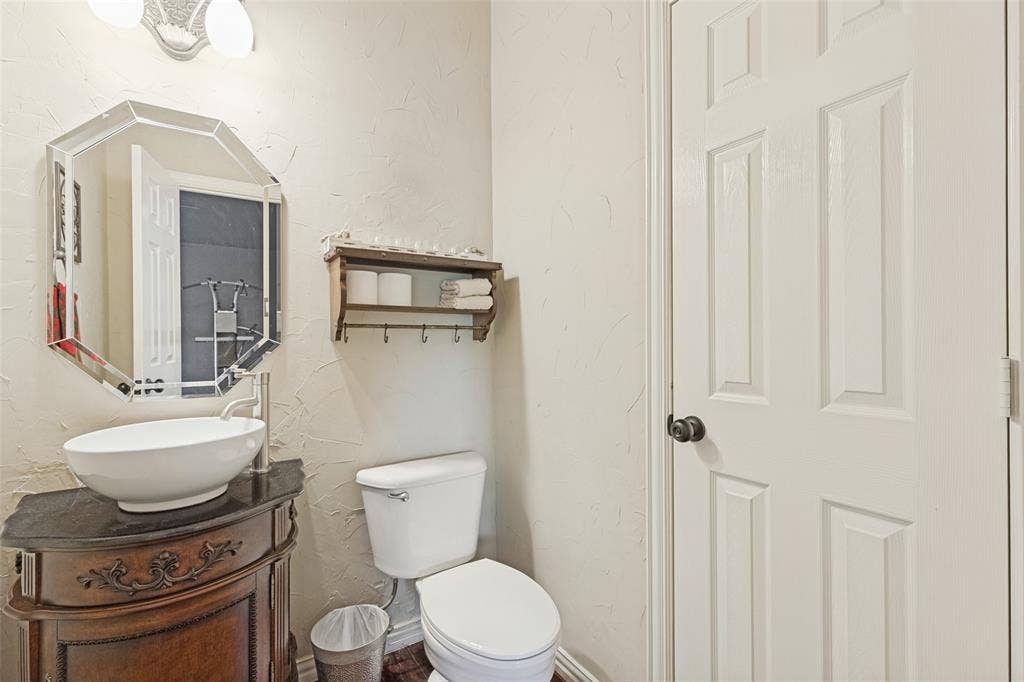2404 Creek Ridge Drive, McKinney, TX 75072 Octagonal wall mirror, vessel sink with high-arc faucet, stone-top vanity, textured wall finish, and six-panel interior door