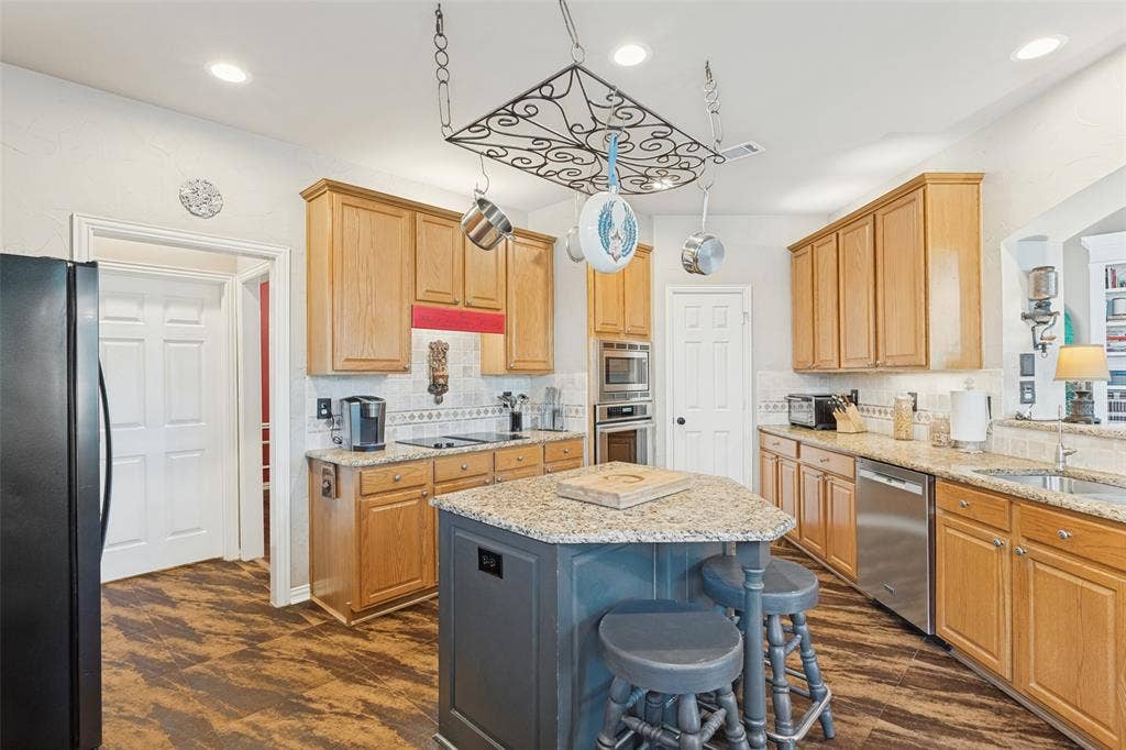 2404 Creek Ridge Drive, McKinney, TX 75072 Kitchen featuring cabinetry with a natural finish, stone countertops, central island, stainless steel built-in oven, and wood-finish flooring