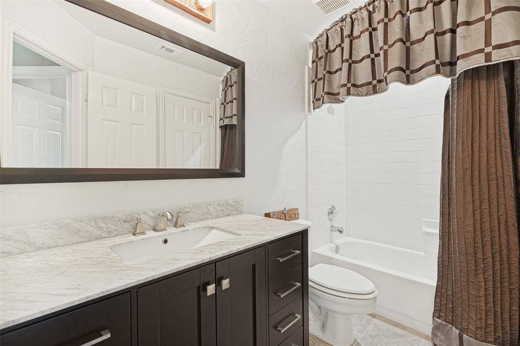 2404 Creek Ridge Drive, McKinney, TX 75072 Bathroom featuring a dark-finish vanity cabinet, stone-surface countertop with an integrated basin, large framed mirror, and a tile-surround shower and tub combination