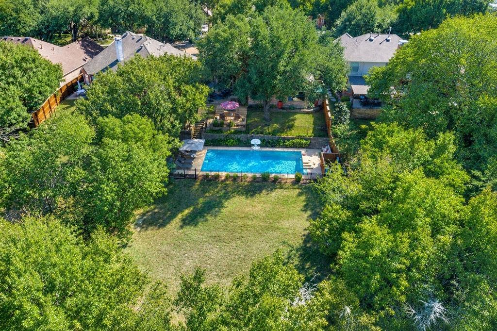 2404 Creek Ridge Drive, McKinney, TX 75072 Expansive backyard featuring an in-ground swimming pool, stone retaining wall, paved patio area, and mature trees