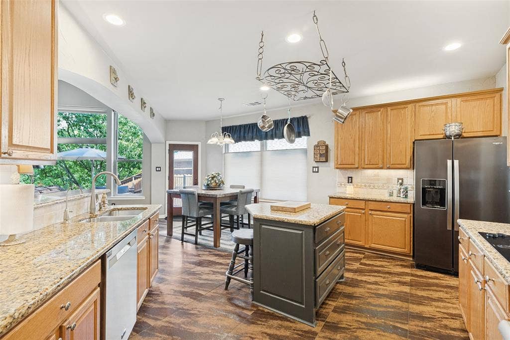 2404 Creek Ridge Drive, McKinney, TX 75072 Kitchen featuring wood cabinetry, stone countertops, wood-finish flooring, a central island with storage, and a ceiling-mounted metal pot rack