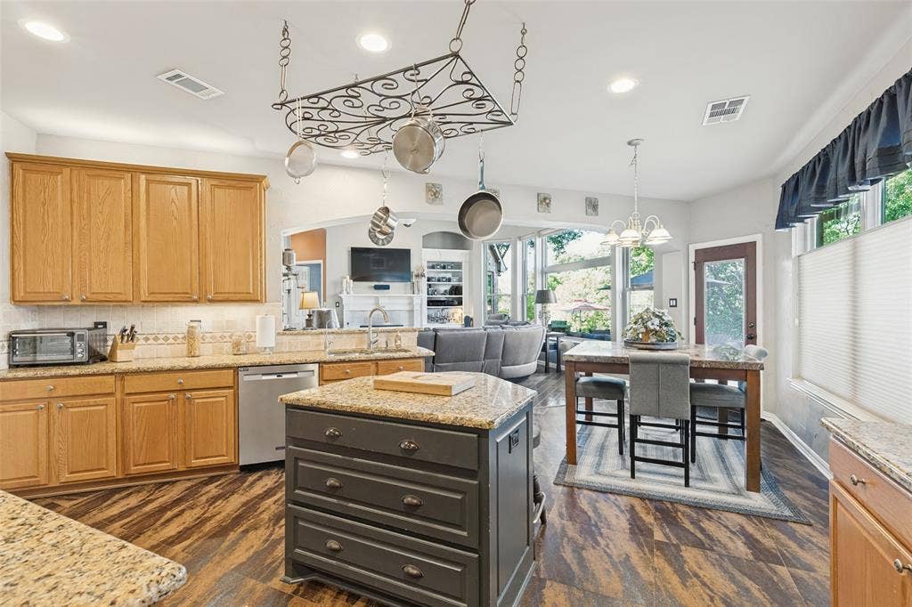 2404 Creek Ridge Drive, McKinney, TX 75072 Kitchen featuring natural-finish wood cabinetry, stone countertops, a central island with storage drawers, decorative metal pot rack, and wood-finish flooring
