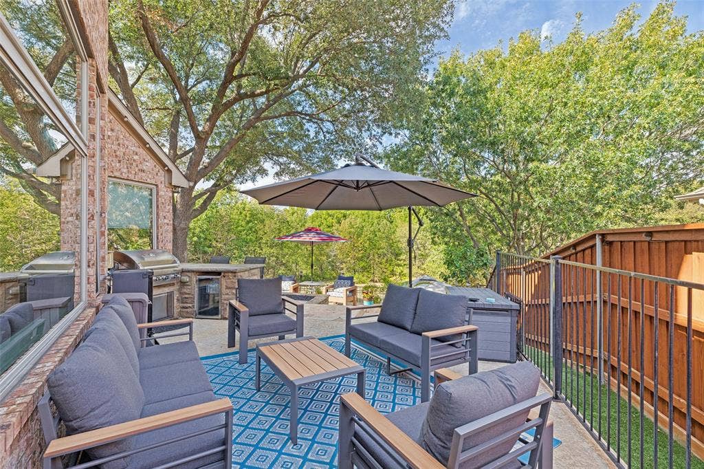 2404 Creek Ridge Drive, McKinney, TX 75072 Outdoor patio featuring a built-in stone grill station, concrete paver flooring, a vertical iron fence, and a brick exterior wall