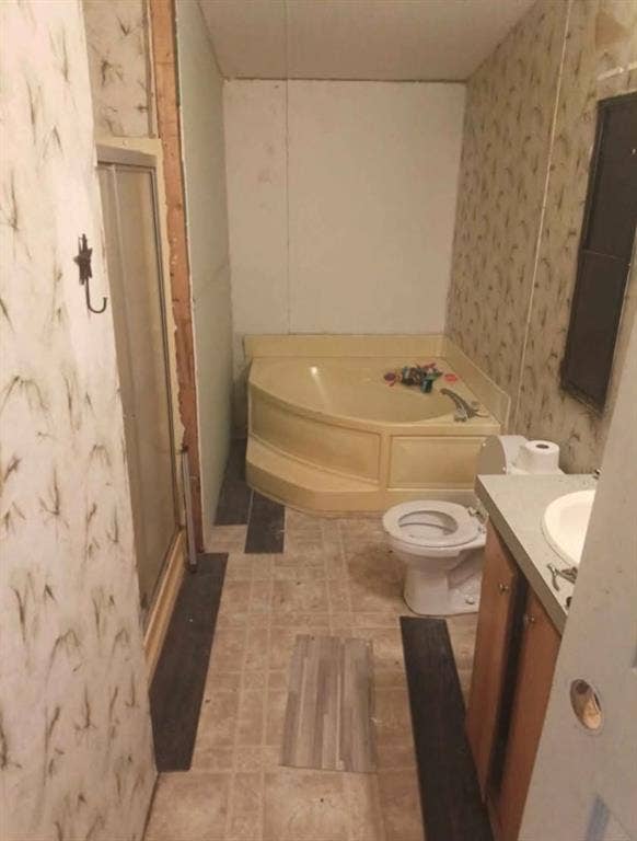 Corner soaking tub with integrated surround, enclosed shower stall, vanity with integrated sink, and dual-finish flooring