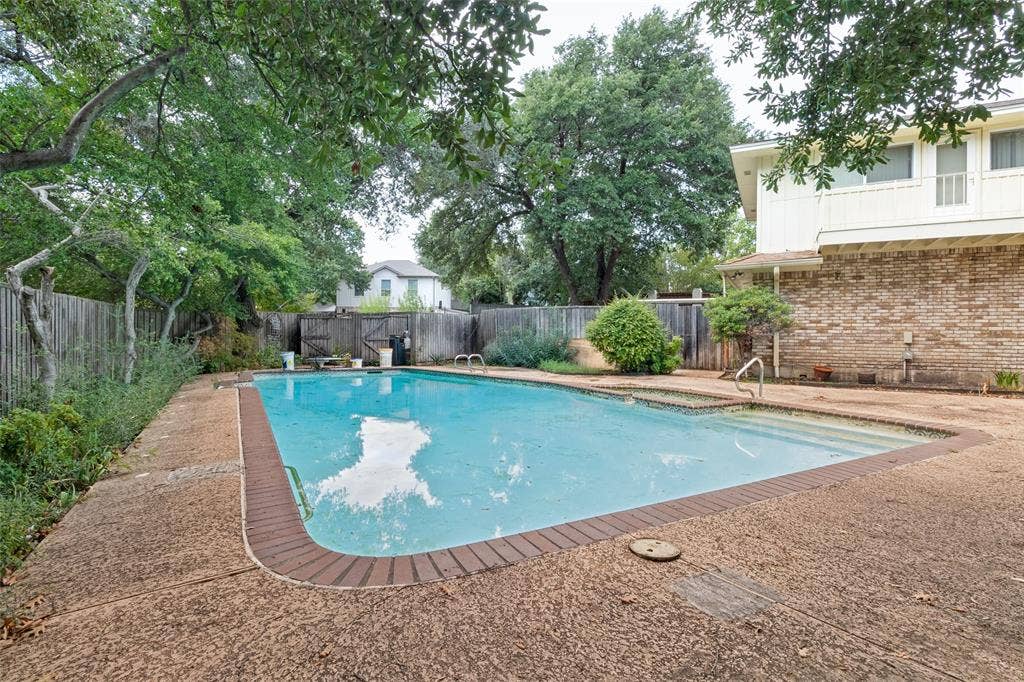 6936 Wildglen Drive, Dallas, TX 75230 In-ground swimming pool with a brick-trimmed edge, aggregate concrete decking, and mature landscaping enclosed by a wood privacy fence