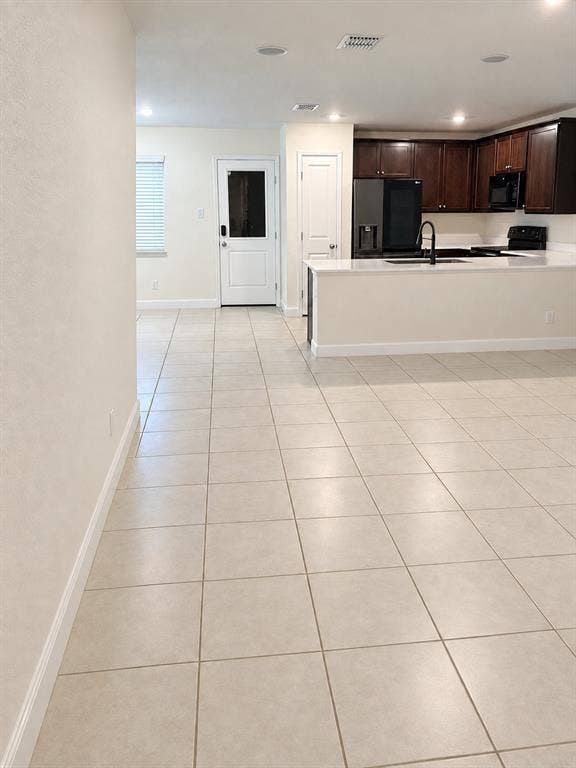 Neutral-tone tile flooring, dark wood-finish cabinetry, white solid-surface countertops, recessed lighting, and a kitchen peninsula