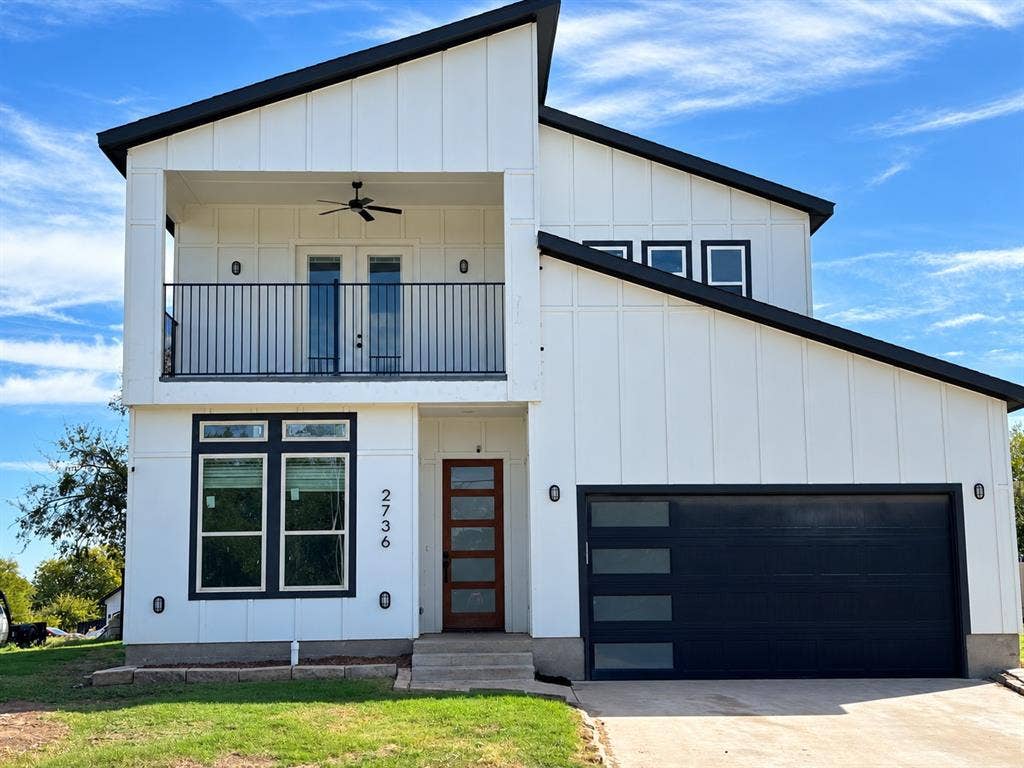 Stunning modern two-story home featuring a striking white board-and-batten exterior, bold black accents, contemporary architectural design, and a spacious two-car garage. The inviting second-story balcony adds charm and character, creating exceptional curb appeal.