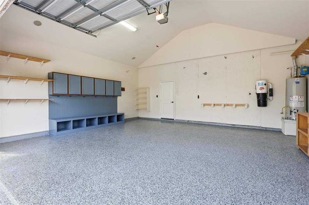 Attached garage featuring an epoxy-coated floor, vaulted ceiling, built-in cabinetry with beadboard detailing, additional wall-mounted shelving, and an integrated central vacuum system