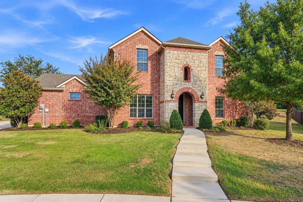Brick and stone exterior facade featuring an arched entryway, gabled rooflines, and a concrete walkway