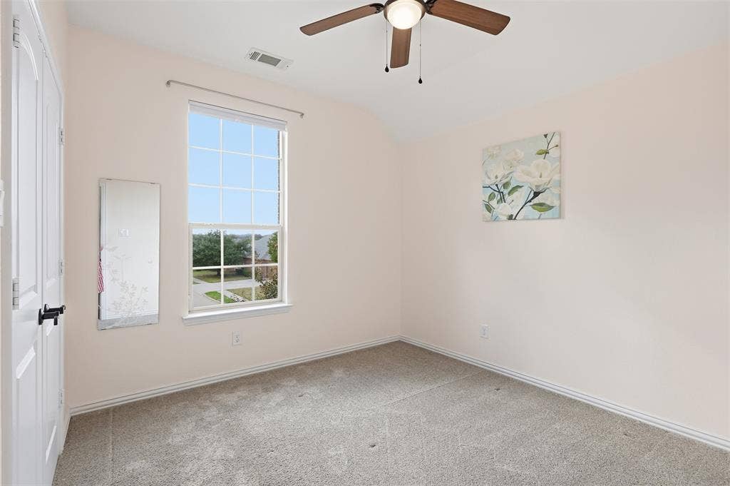 Room featuring neutral wall tones, carpeted flooring, a grid-patterned window, and a ceiling fan with integrated lighting