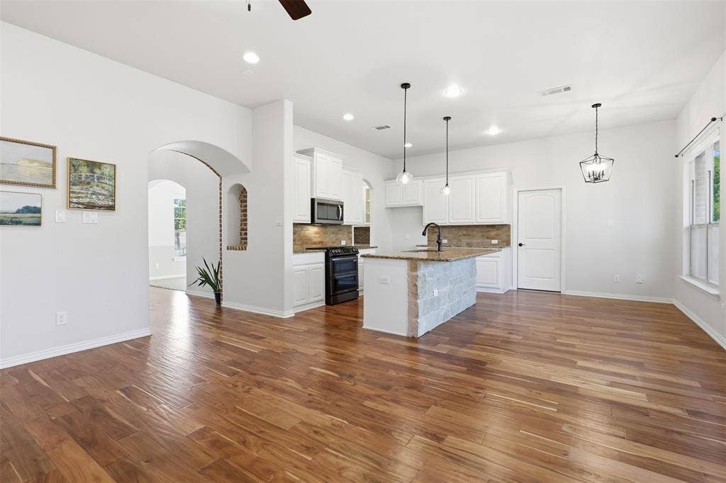 Kitchen featuring white cabinetry, wood-finish flooring, a stone-accented center island with countertop seating, recessed lighting, and a brick-lined arched architectural niche